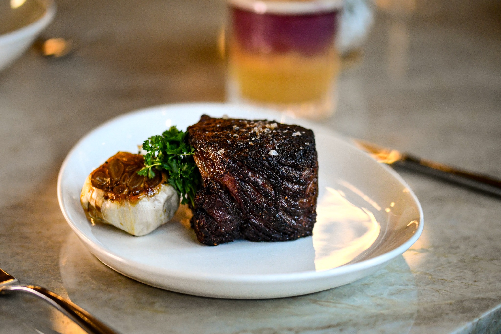Restaurant steak presentation with a cocktail softly blurred in the background